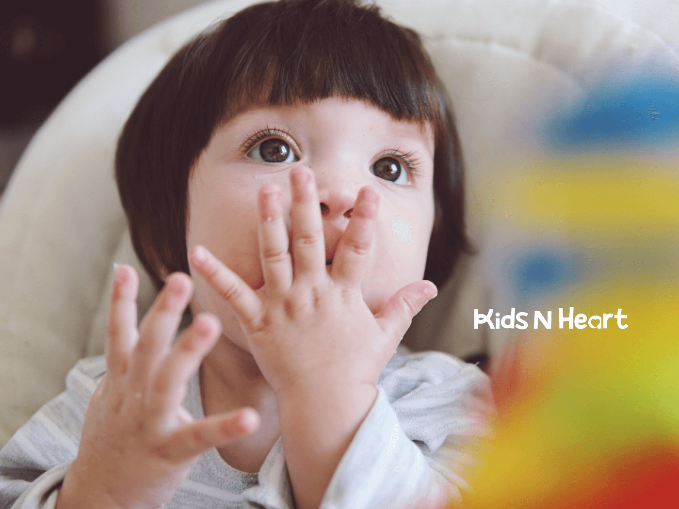 Close-up of curious baby with hands near mouth, exploring textures while sitting in a high chair at home during sensory play
