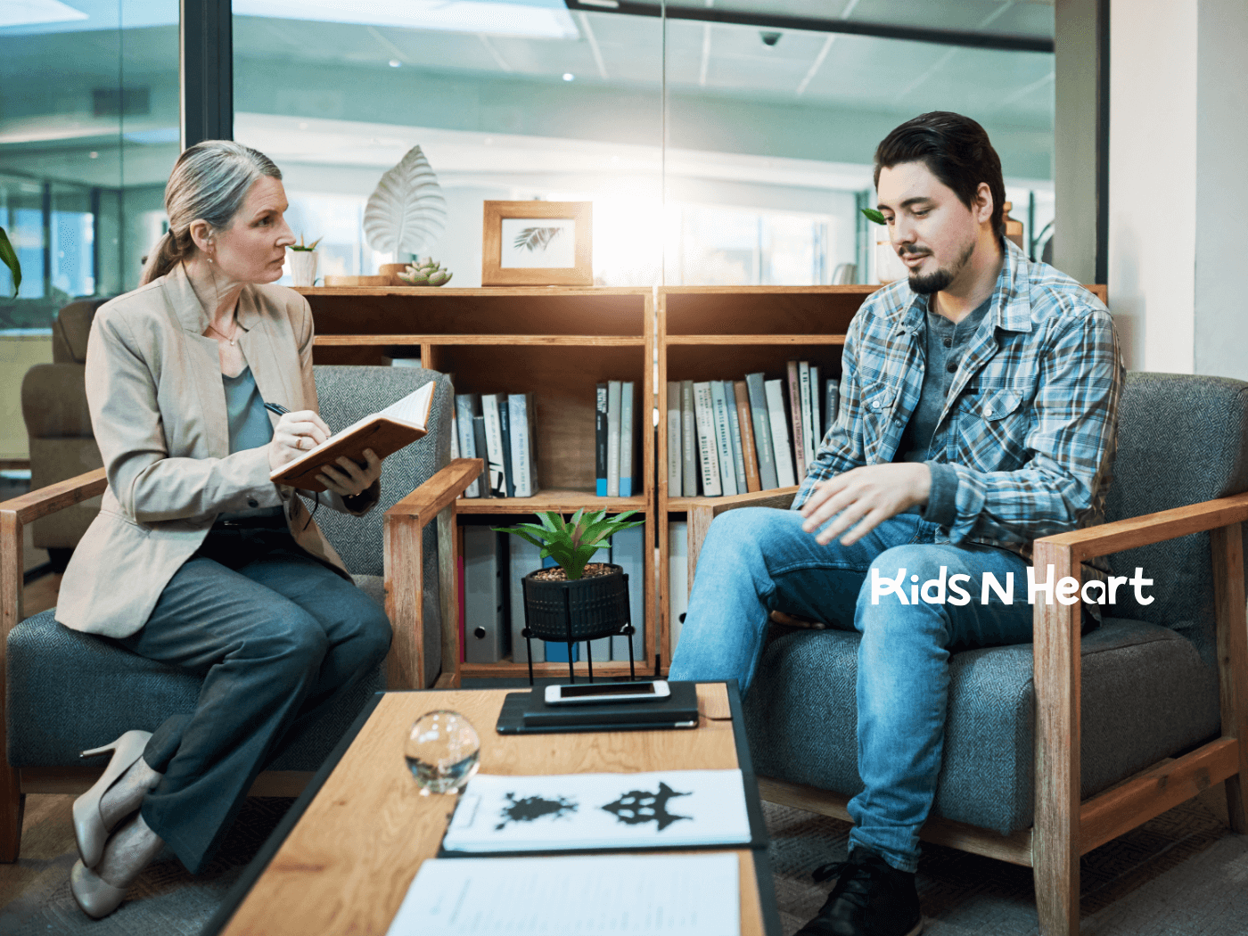 Therapist takes notes while listening to an adult client during a calm counseling session in a modern office.