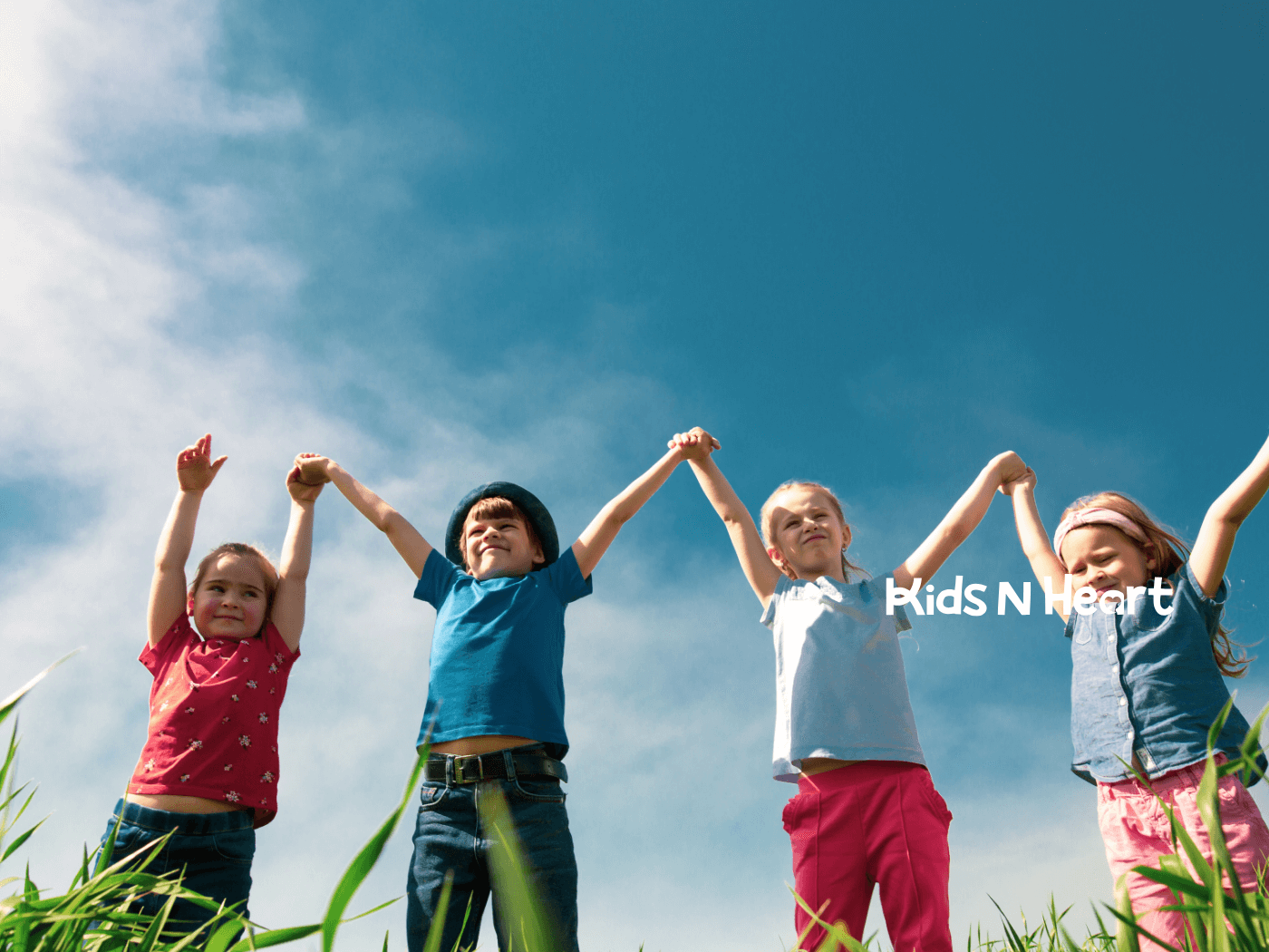 Group of young children holding hands outdoors under a blue sky, celebrating inclusion, friendship, and joyful play together.