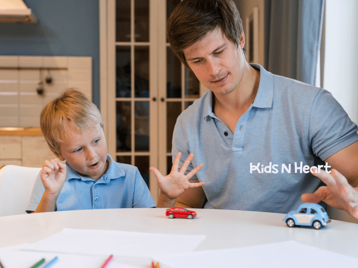 Father and young child play with toy cars at a table, modeling turn-taking and communication skills at home.