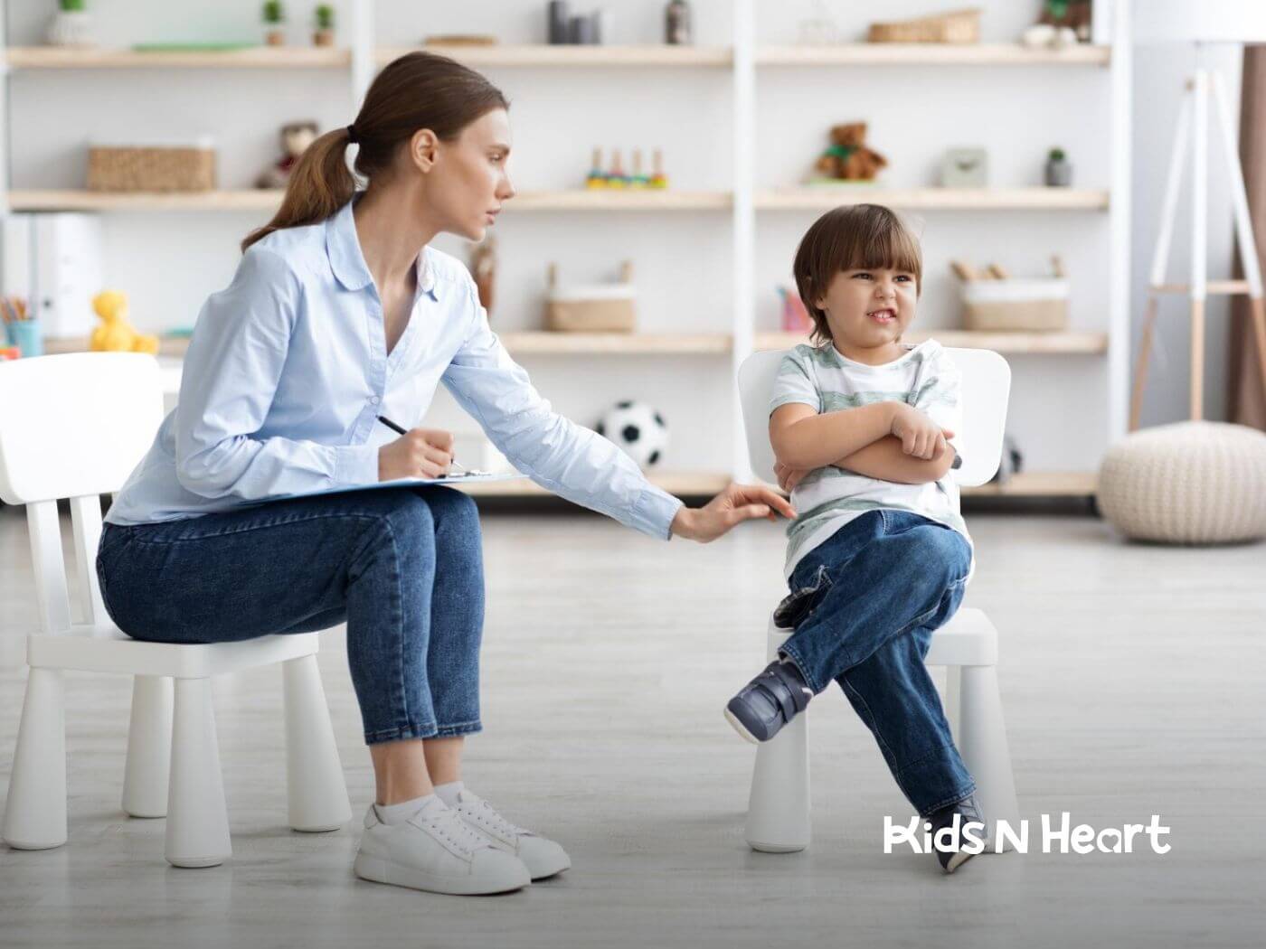 A child with crossed arms sits as an ABA therapist takes notes.