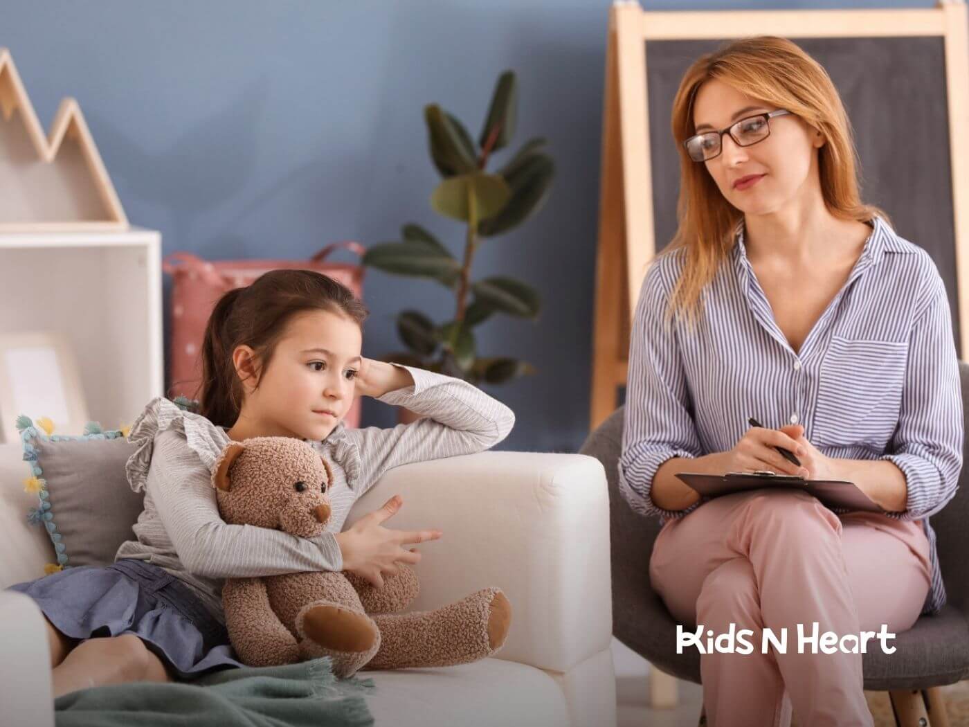 An autistic holds a teddy bear while an ABA therapist writes nearby.