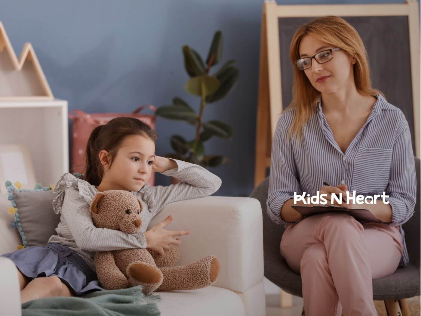 An autistic holds a teddy bear while an ABA therapist writes nearby.