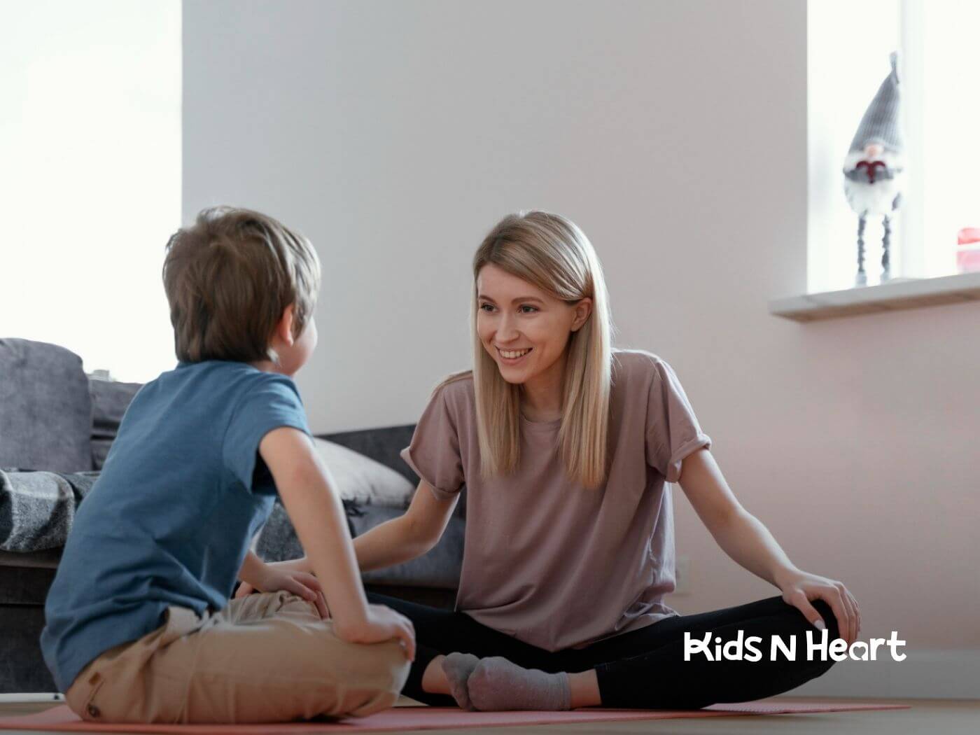 An ABA therapist smiles at a boy sitting on the floor in ABA therapy.