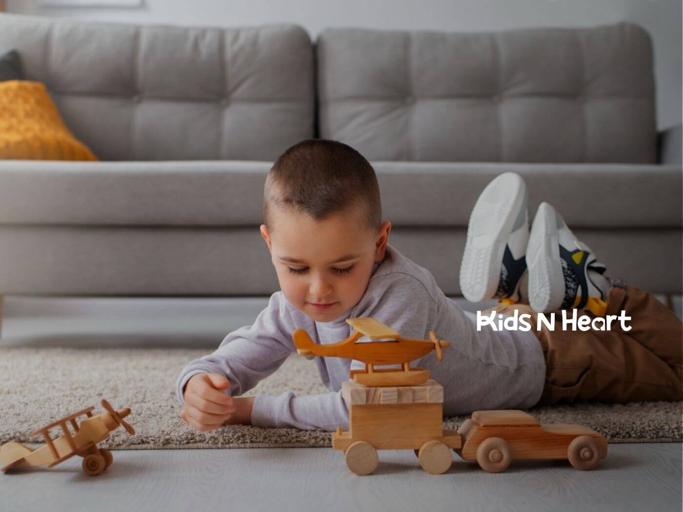 A boy with autism lying on the floor focused on wooden toy airplanes and cars.