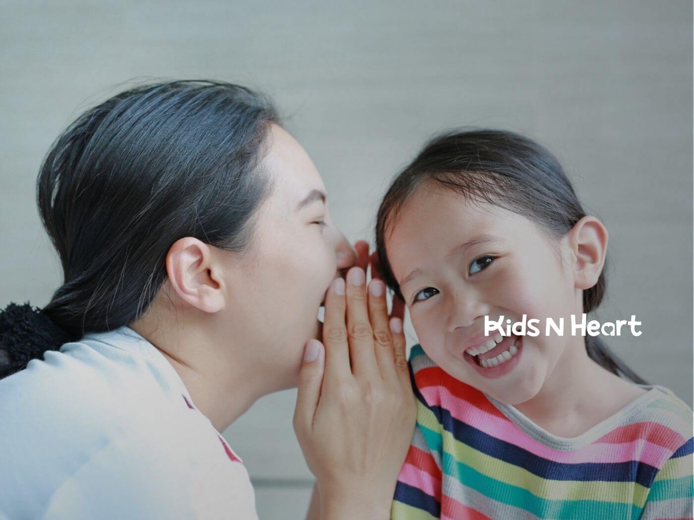 An ABA therapist whispering to a smiling girl in a striped shirt during ABA therapy.