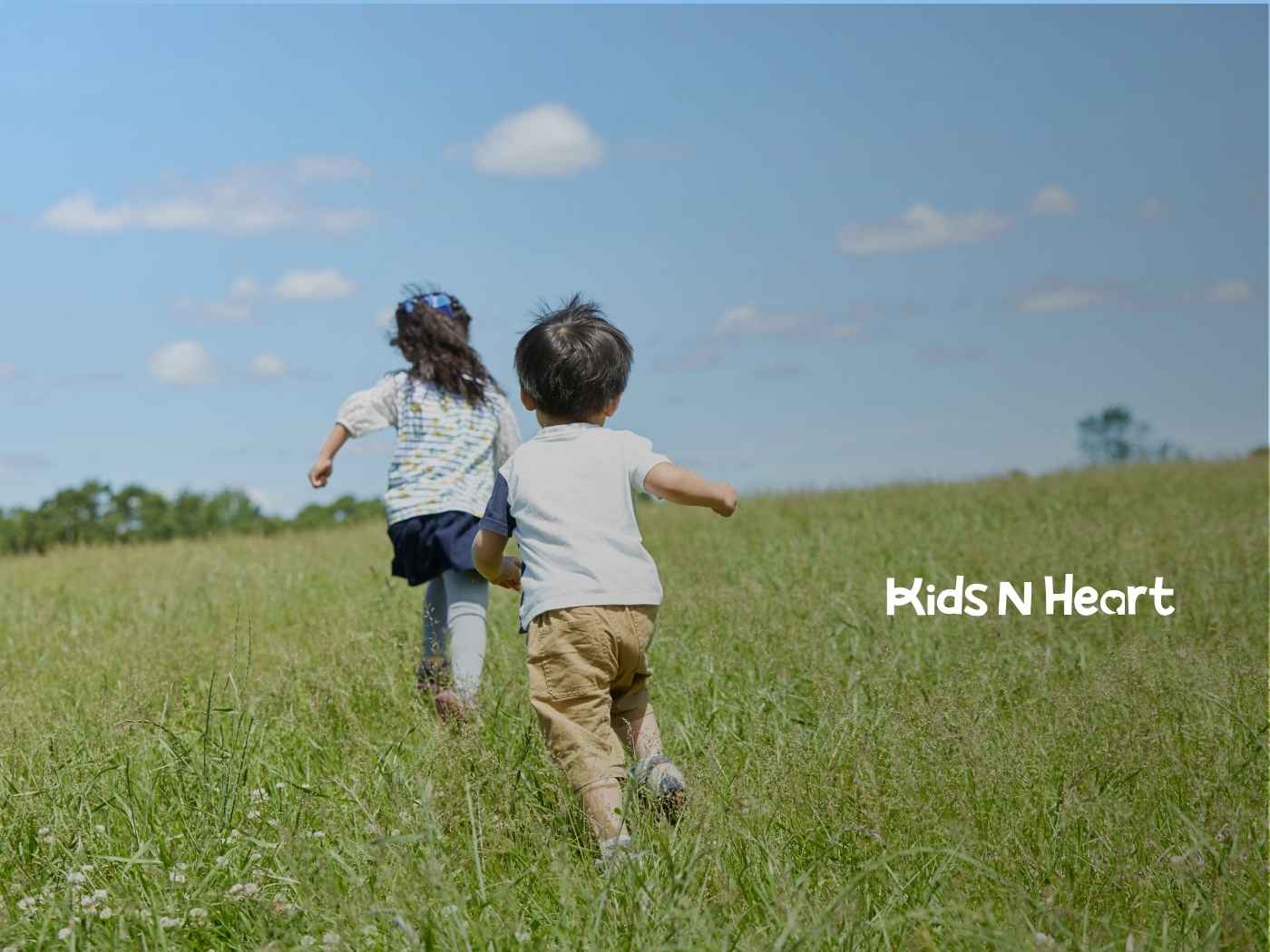 Two children run through a sunlit meadow under a clear blue sky, conveying joy and freedom.