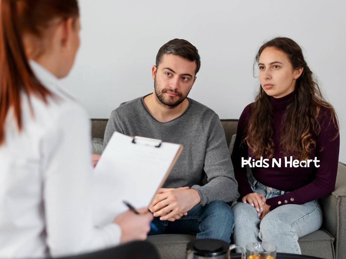 A couple sits on a couch while ABA therapist takes notes during ABA parent training.