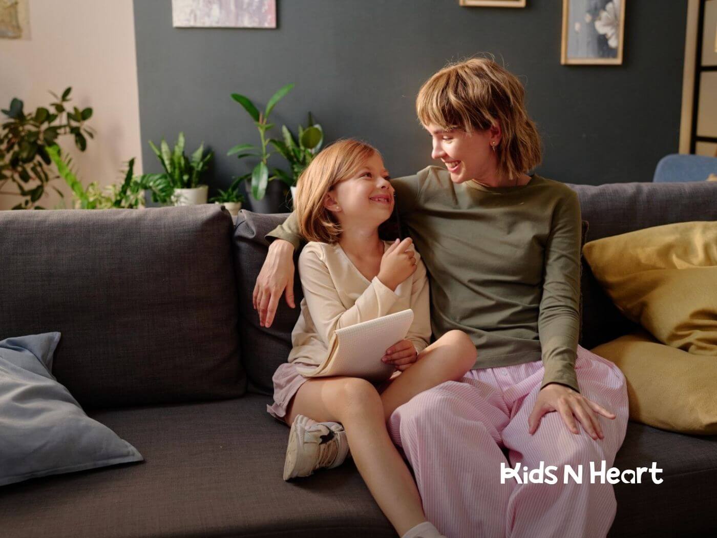 Therapist and girl with autism smile together on a couch at home during ABA therapy.