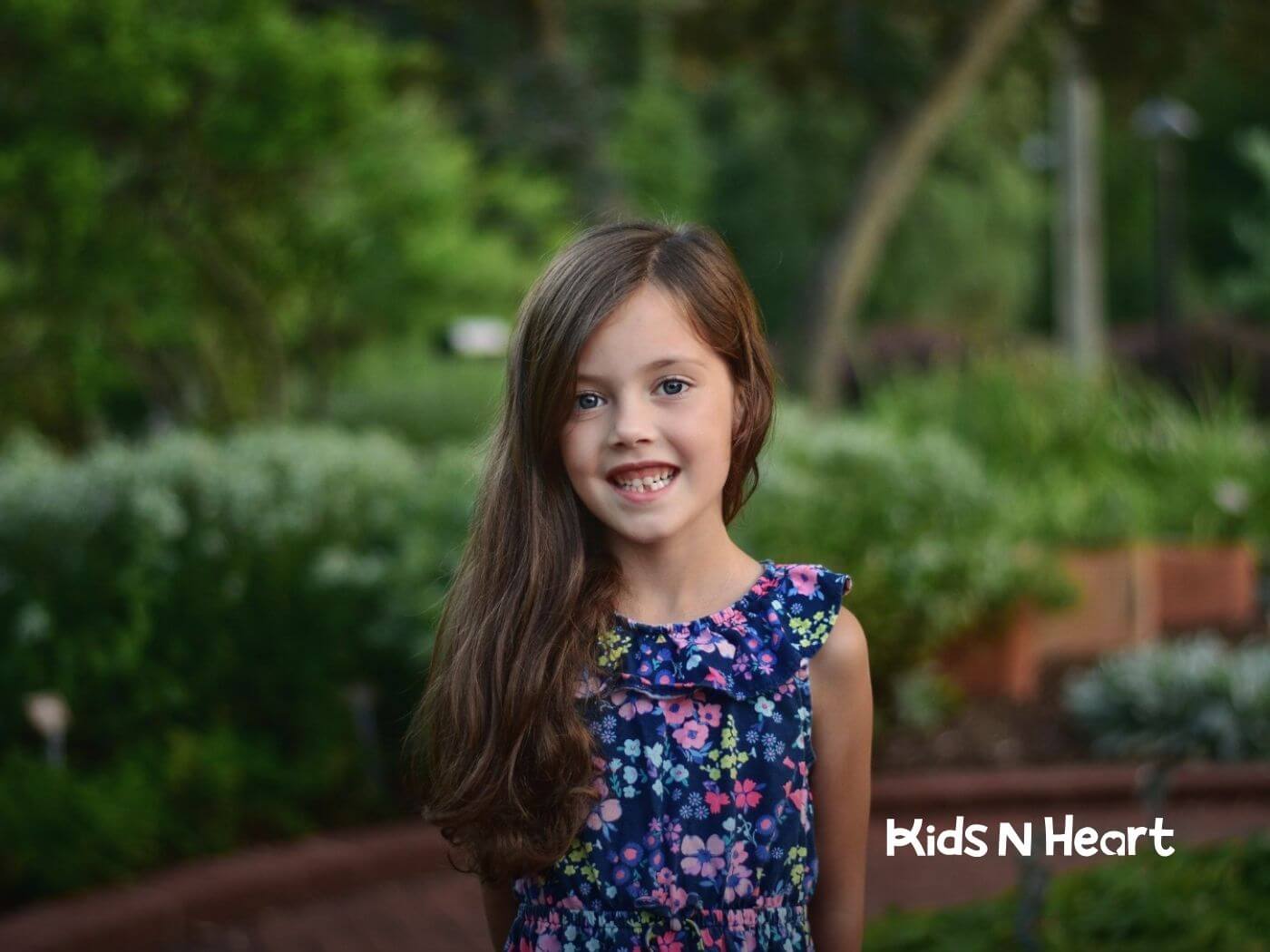 A young girl with autism smiling in a garden with a floral dress after ABA therapy session.