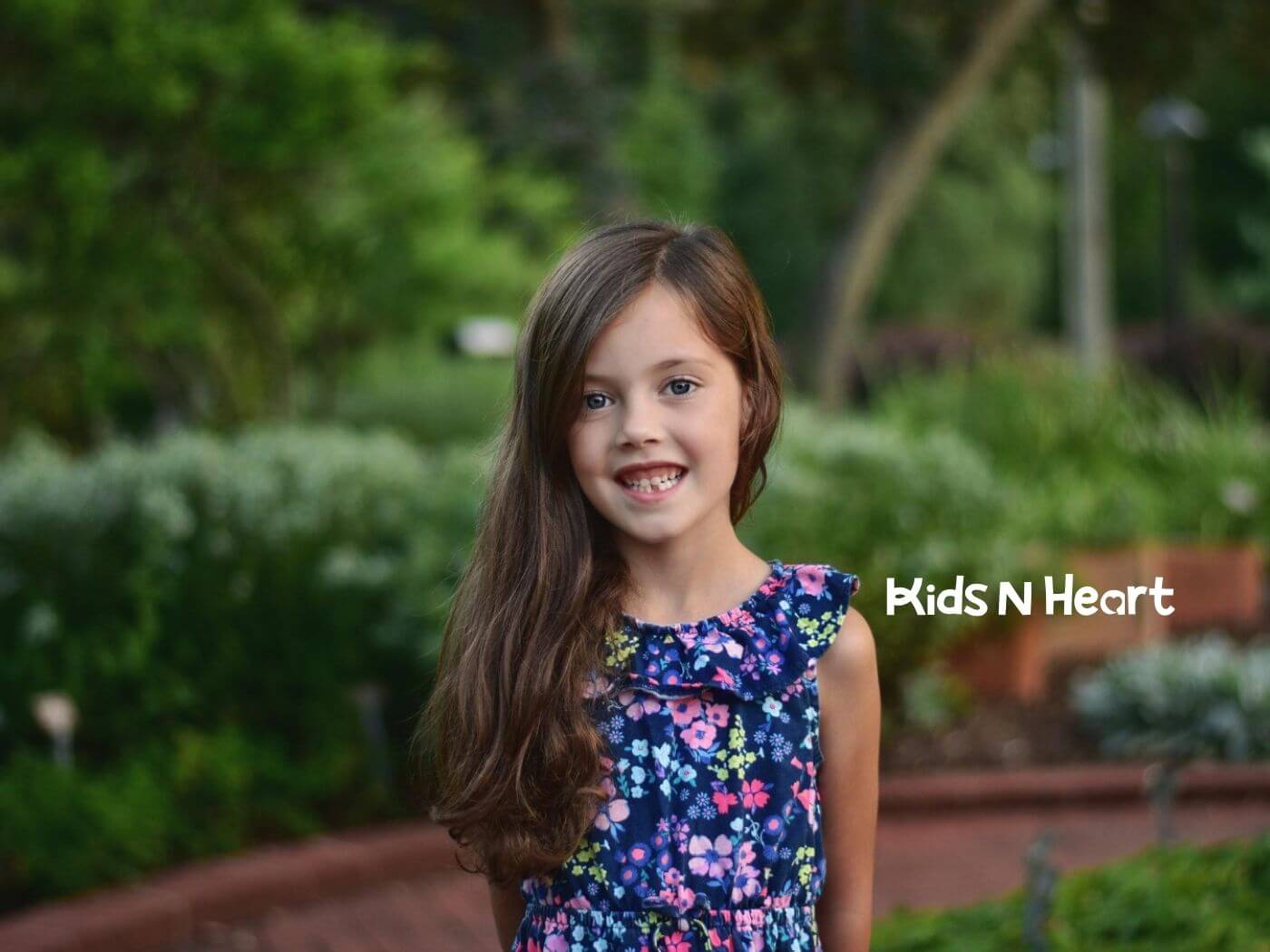 A young girl with autism smiling in a garden with a floral dress after ABA therapy session.