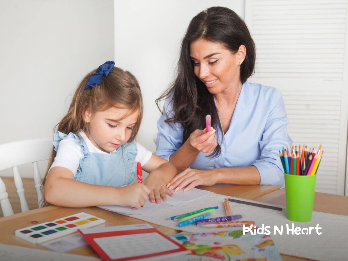 Therapist and young girl with autism sit at a table drawing and coloring with markers and colored pencils.