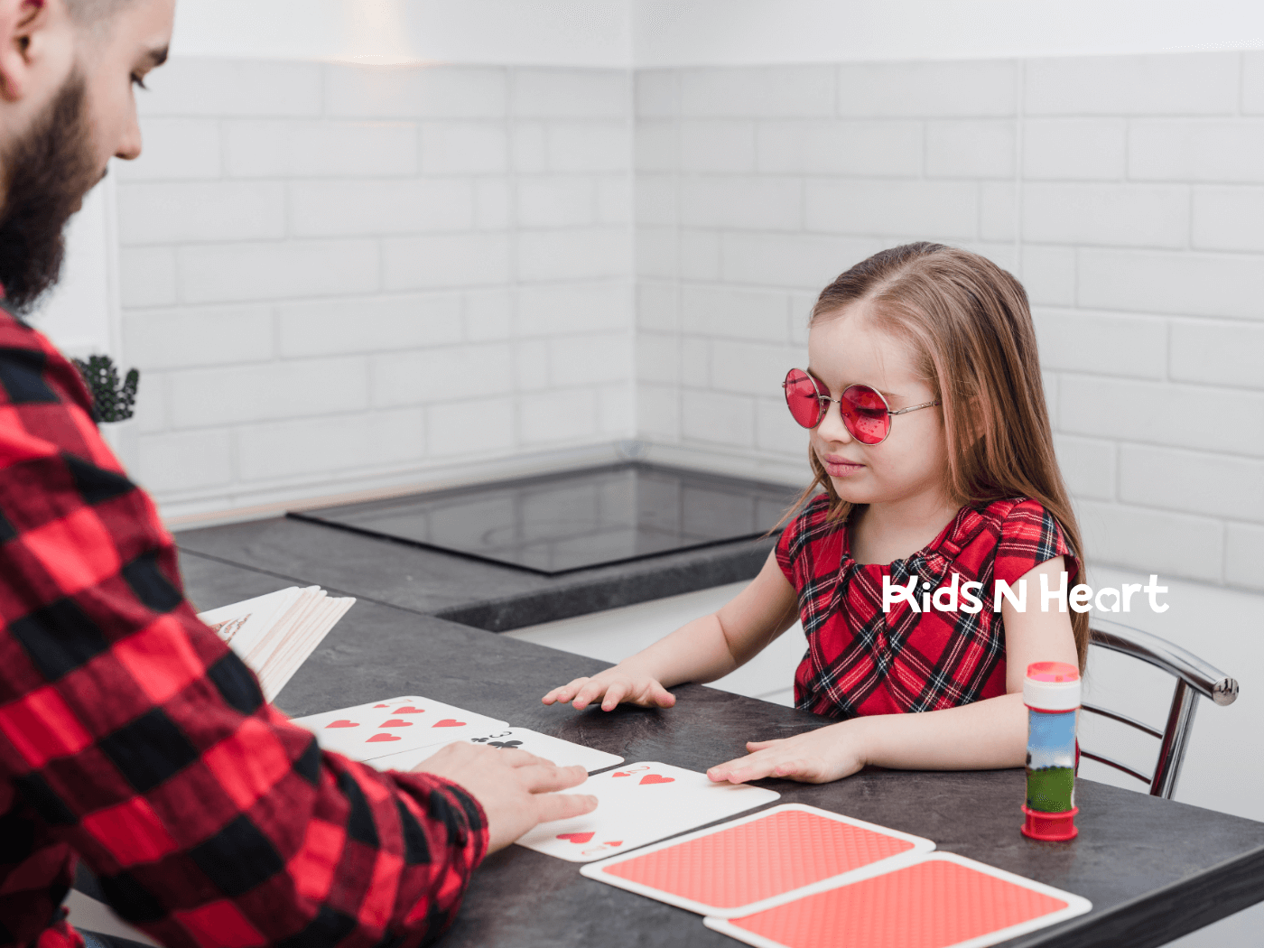 An autistic child wearing red sunglasses sitting at a table, playing card games with an adult after ABA therapy.