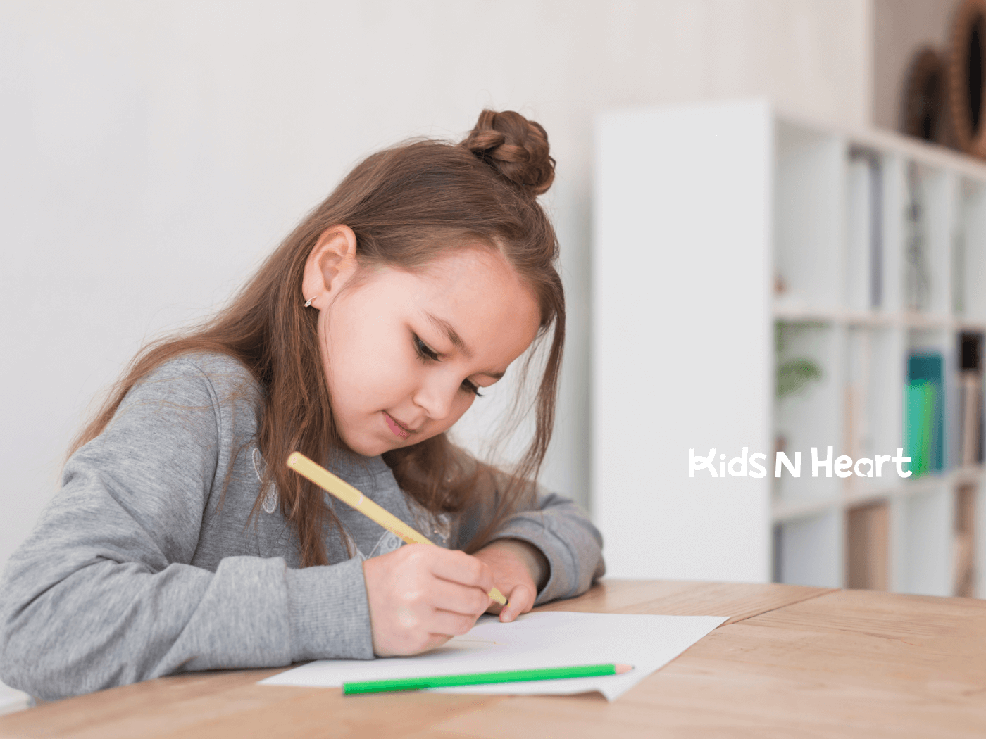A young girl focused on drawing, sitting at a table with colored pencils and a white sheet of paper.
