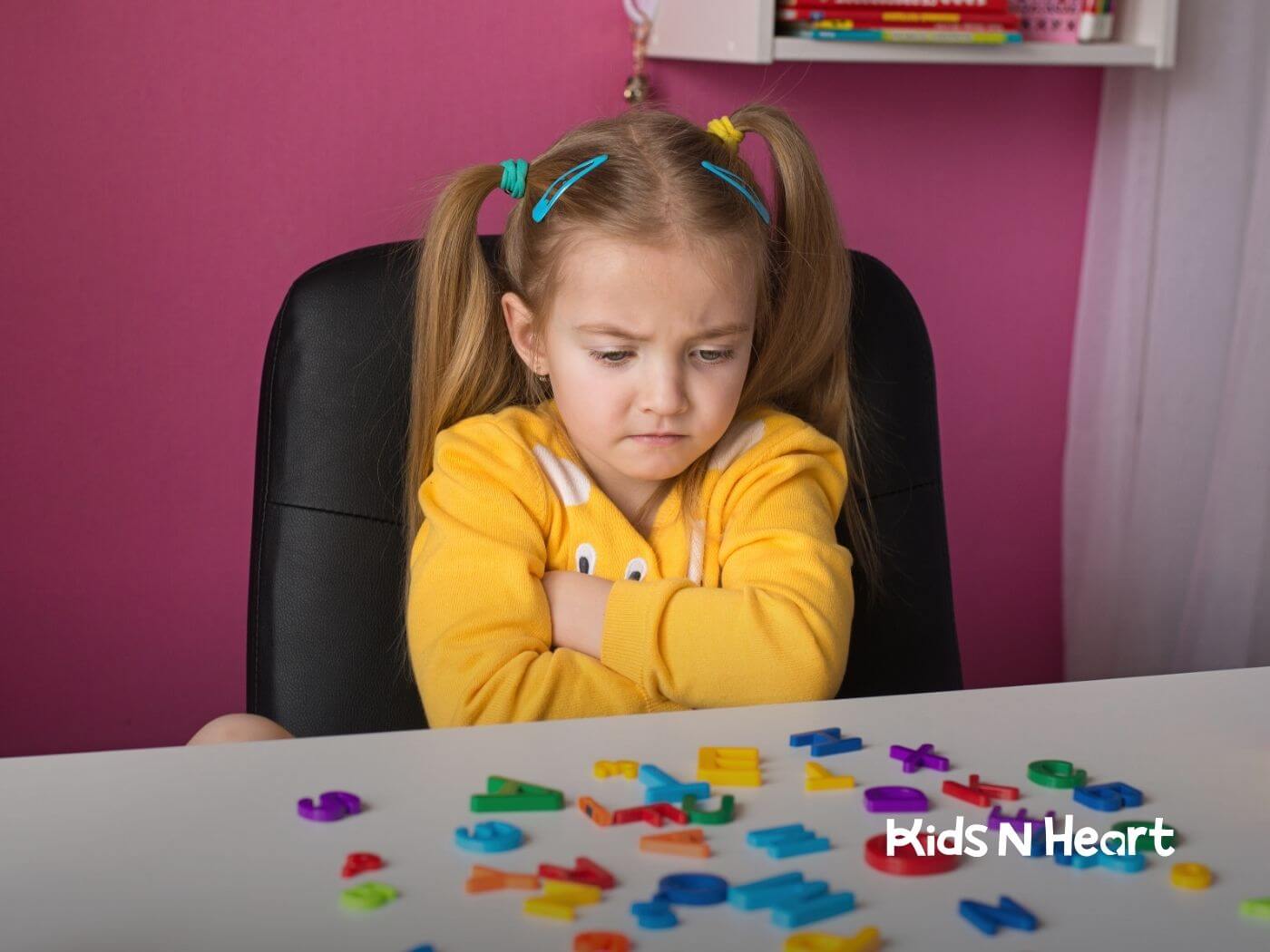 The autistic girl with crossed arms looking frustrated while sorting colorful alphabet magnets during ABA therapy.