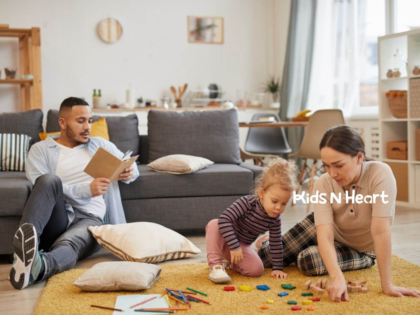 Family sitting on the floor at home while a toddler plays with toys.