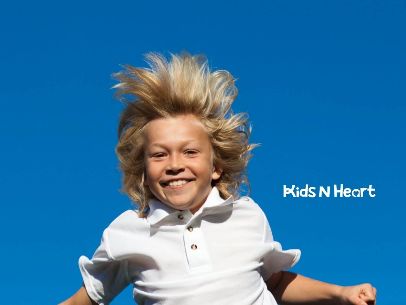 Smiling child with autism jumping with arms outstretched against a blue sky.