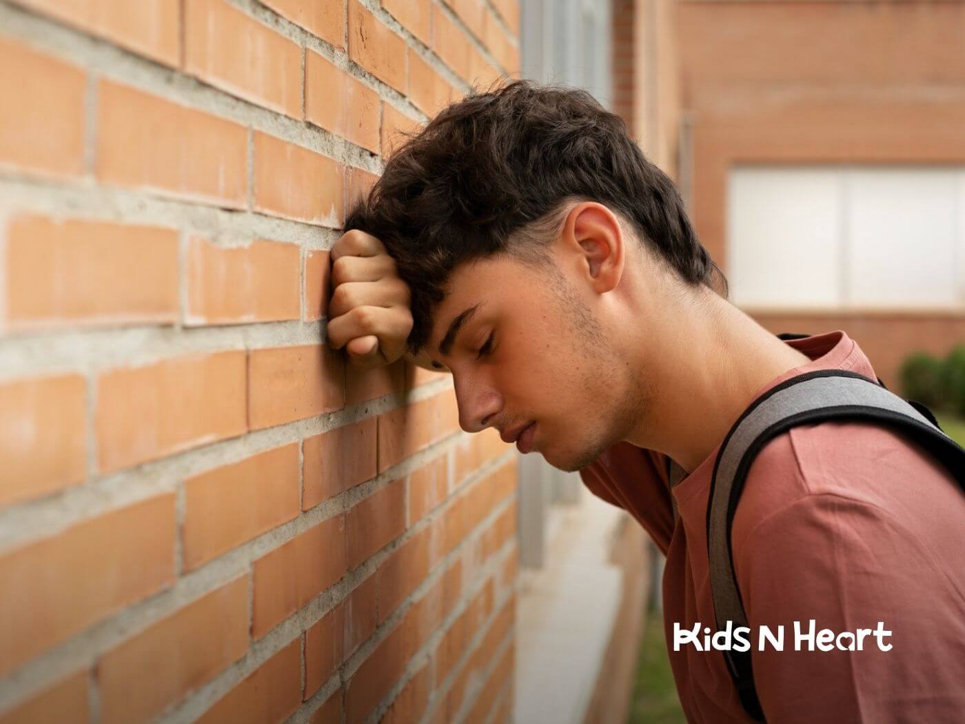 Autistic teenager with a backpack leaning against a wall, looking stressed.