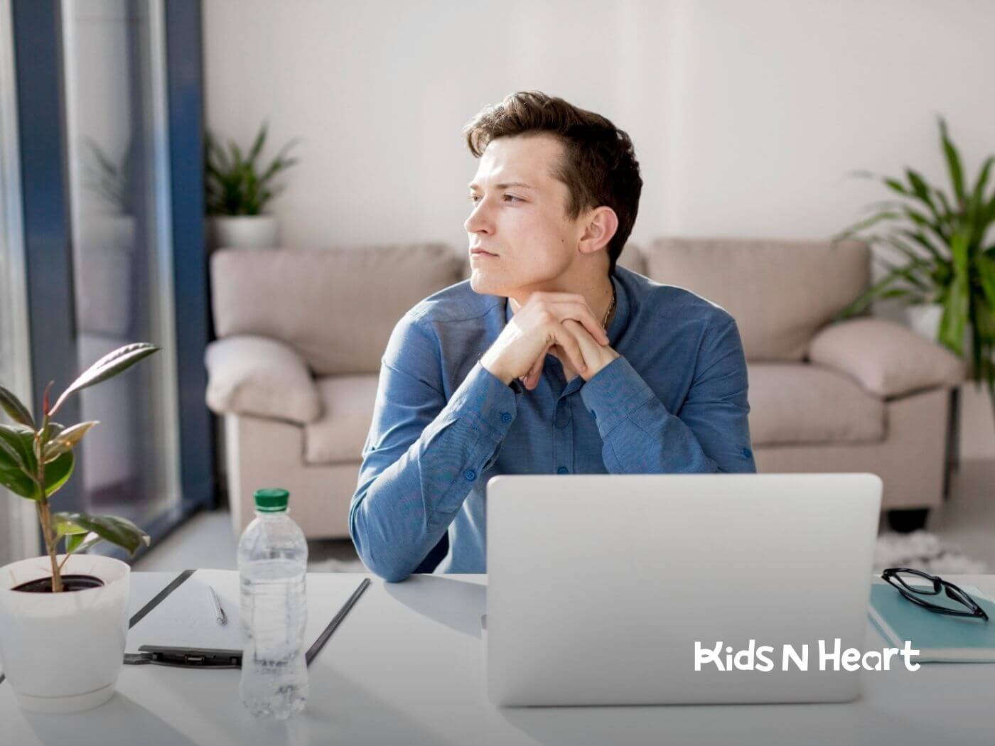 Man with autism sitting at a desk, looking thoughtful while working on his laptop.