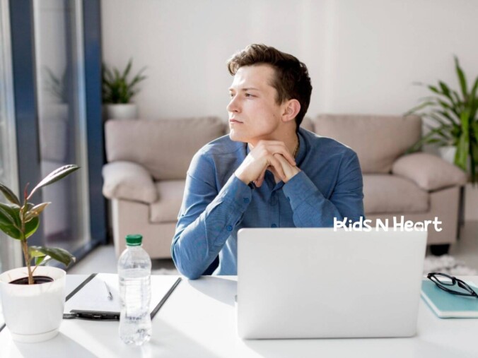 Man with autism sitting at a desk, looking thoughtful while working on his laptop.